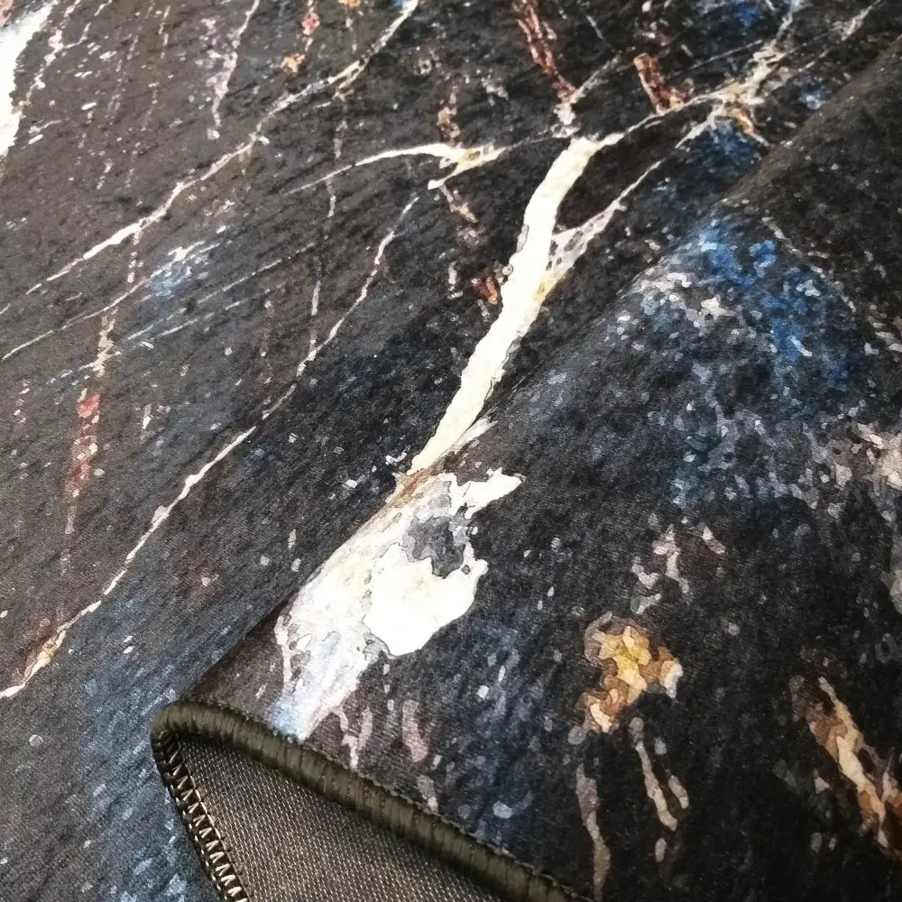 Svart og gull teppe 120 x 180 cm, nærbilde som viser marmormønster, synlig tekstur og kantens søm.