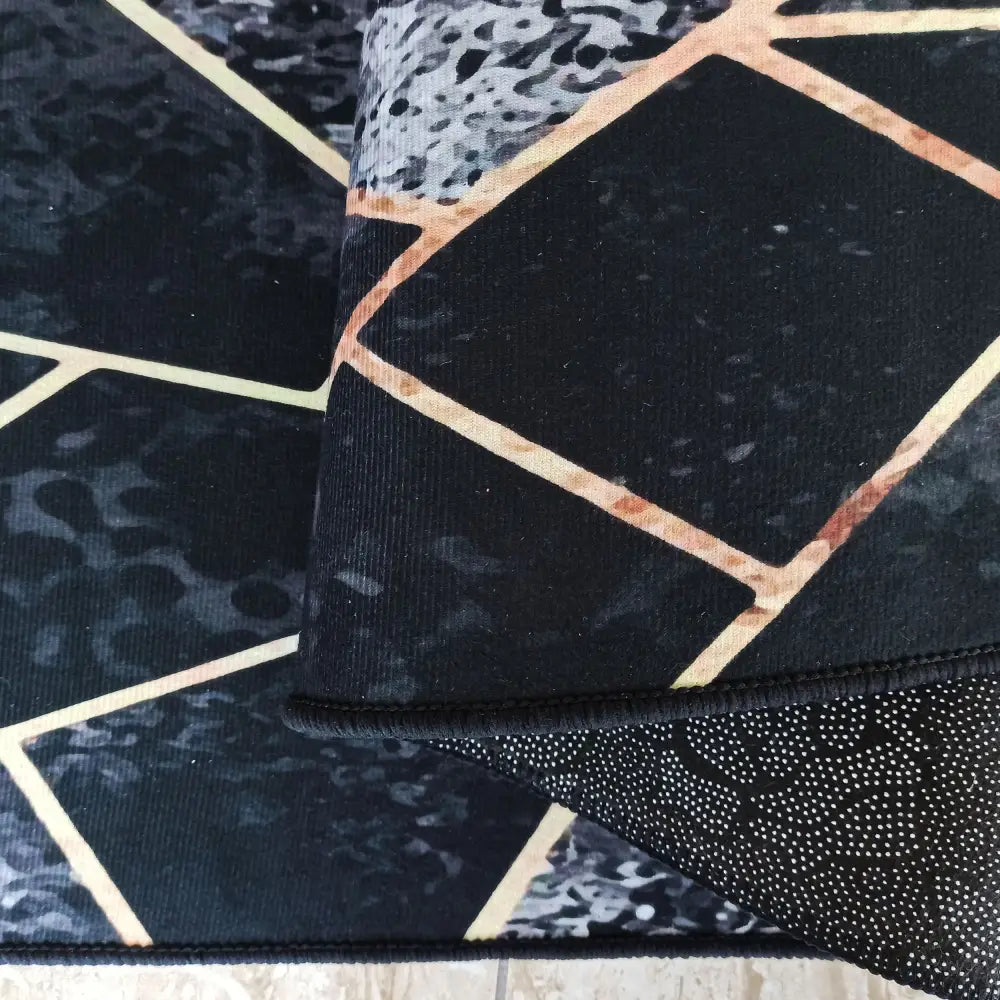 Svart og gull Tepe teppe, nærbilde som viser geometrisk mønster, gullstriper og lodden underside i hjørnet.