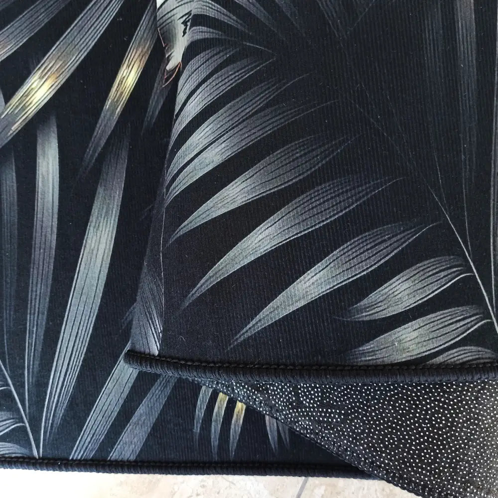 Svart og gull teppe 160x220 cm, nærbilde av grå bladmønster og underside med små hvite prikker.