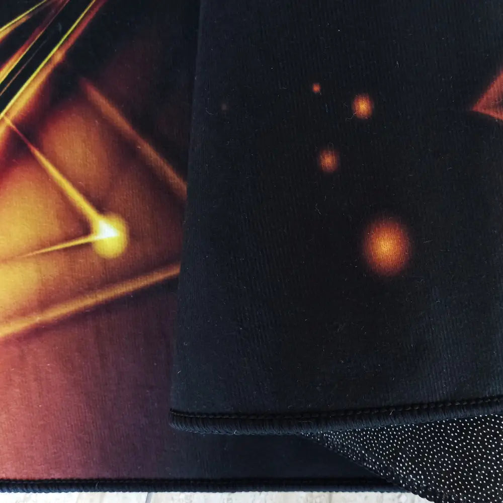 Svart og gull Tepe N14 teppe, nærbilde av brettet hjørne med gummiert underside og grafisk mønster.