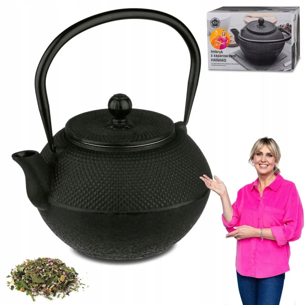 Svart tekanne i støpejern med strukturert overflate, kvinne peker mot kannen, eske og løs te synlig.