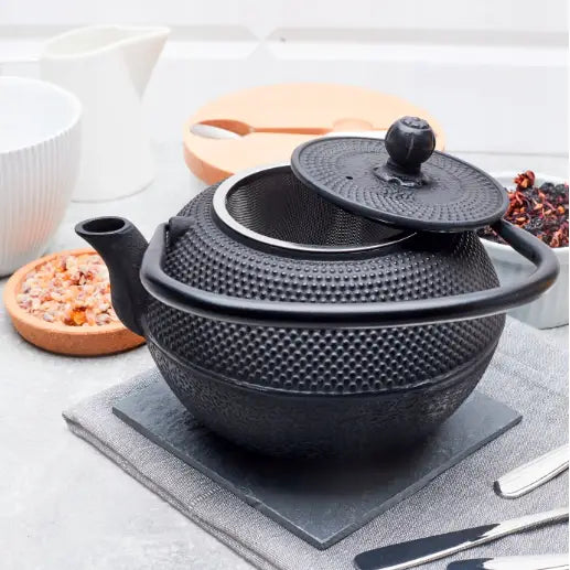 Svart tekanne i støpejern med åpent lokk og synlig tefilter, strukturert overflate og kraftig håndtak.