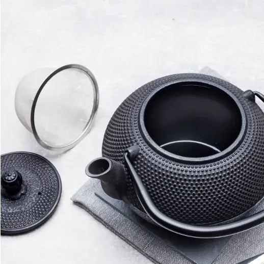 Svart tekanne i støpejern sett ovenfra, med avtagbart lokk, tesil og strukturert overflate.