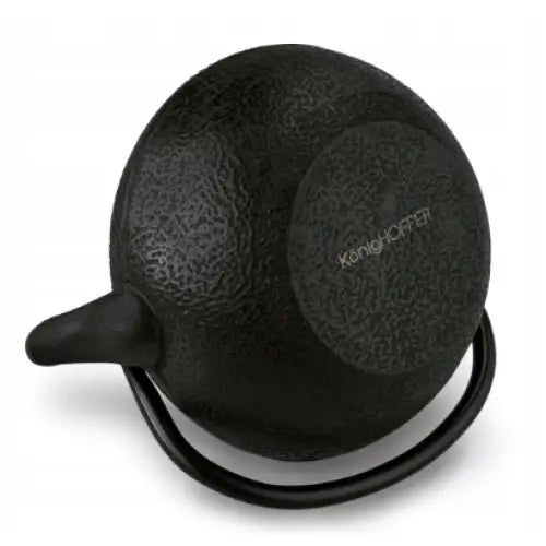 Svart tekanne i støpejern sett ovenfra, grov tekstur og synlig logo midt på lokket.