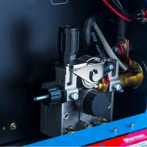 Sveiseapparat detalj, nærbilde av justeringsskruer, hjul og ledninger mot sort bakgrunn med blå kant.