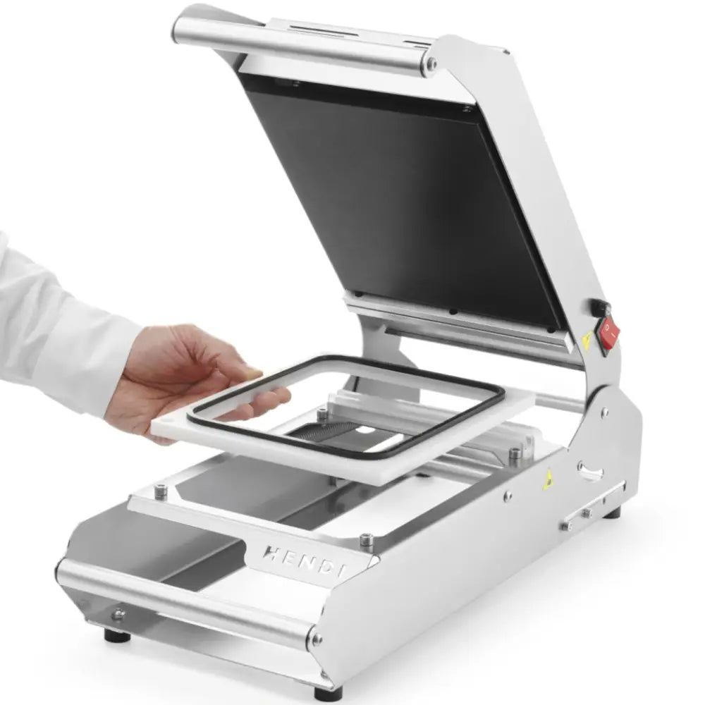 Sveisemaskin for brett og kopper, lokket åpent, hånd posisjonerer ramme over den sorte innsiden.