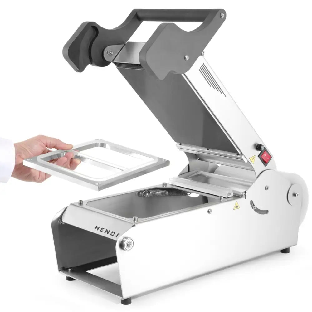 Sveisemaskin for takeaway matbeholdere, sidevisning med åpent lokk og ramme løftet over maskinen.