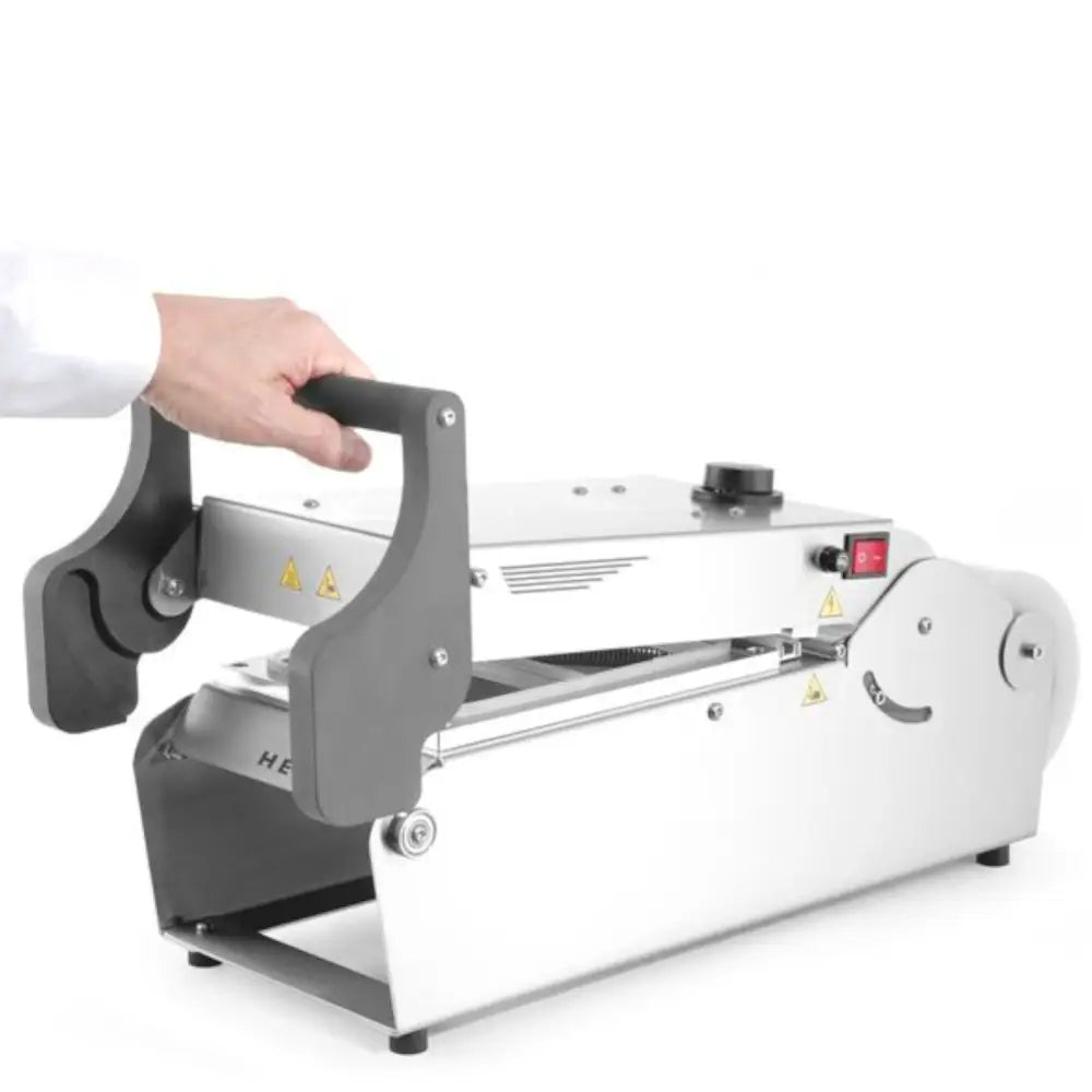 Sveisemaskin for takeaway matbeholdere, skråvisning med hånd på håndtak og synlige advarselsmerker.