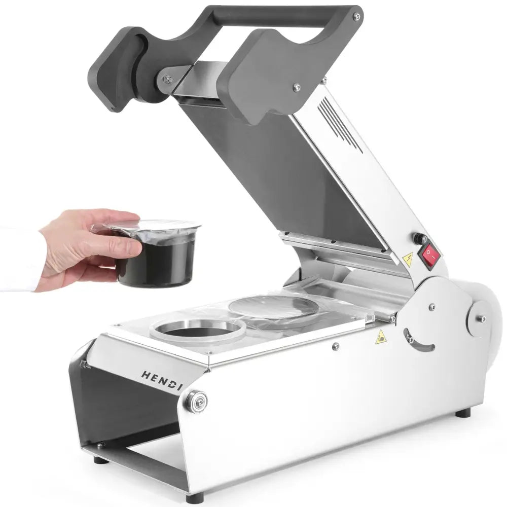 Sveisemaskin for takeaway matbeholdere, åpent lokk, hånd plasserer plastbeger i maskinens åpning.