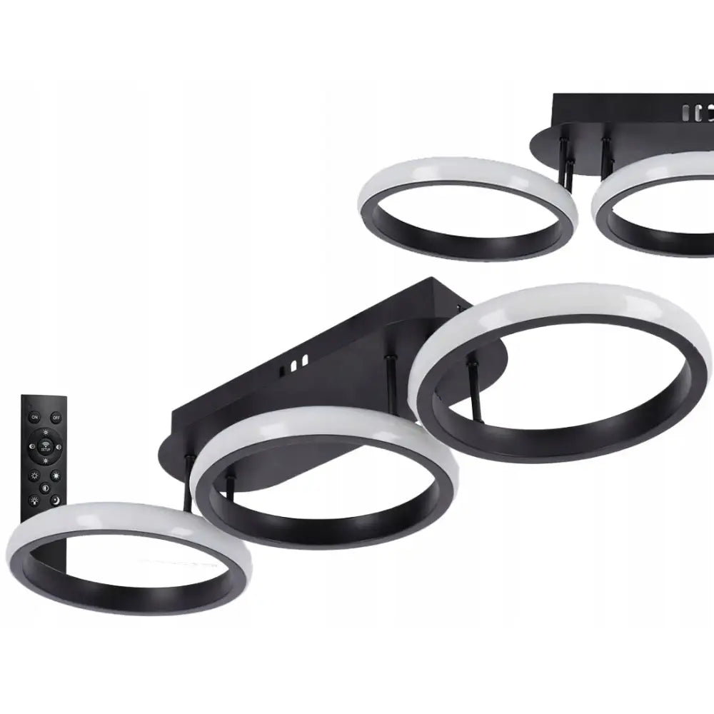 Taklampe med fire LED-ringer i sort og hvitt, moderne utforming, fjernkontroll synlig til venstre.