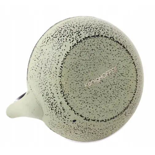 Lysegrønn Konighoffer kopp i keramikk sett fra undersiden, med mørke prikker og synlig hank til venstre.