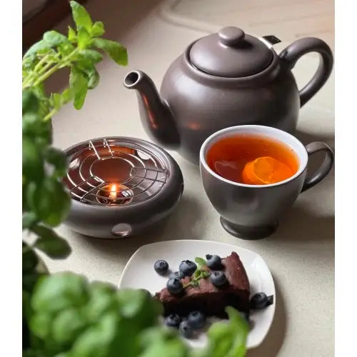 Tekanne med infuser i grått steintøy, servert med te, kake og blåbær på asjett, varmeplate med telys.