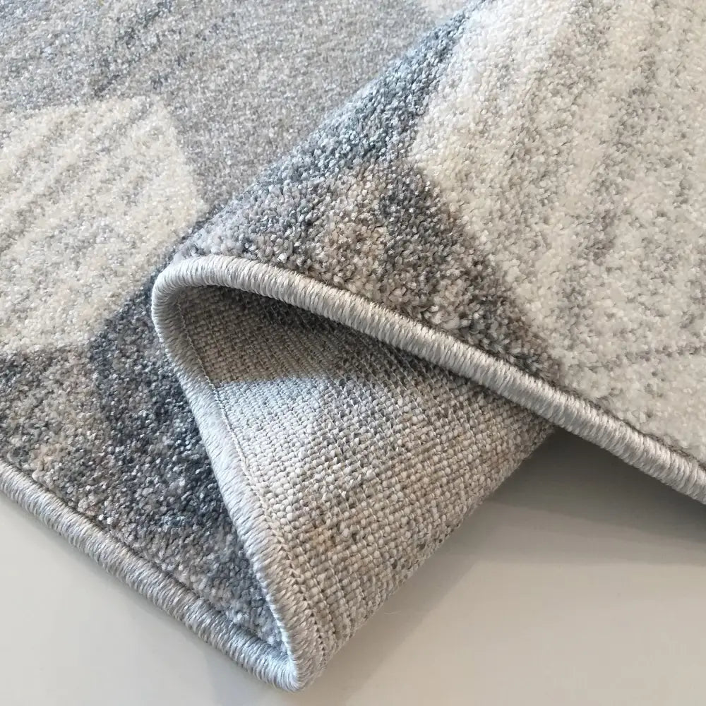 Tepe teppe grå 240 x 330 cm, nærbilde av oppbrettet hjørne med mønstret overside og slitesterk bakside.