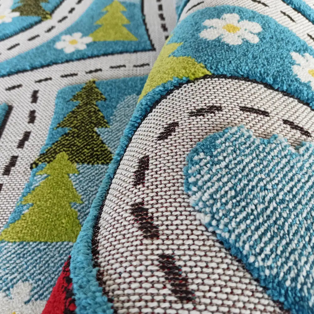 Tepe Barn Color 02 blått teppe, nærbilde av veimotivet med trær, blomster og synlig strukturert kant.