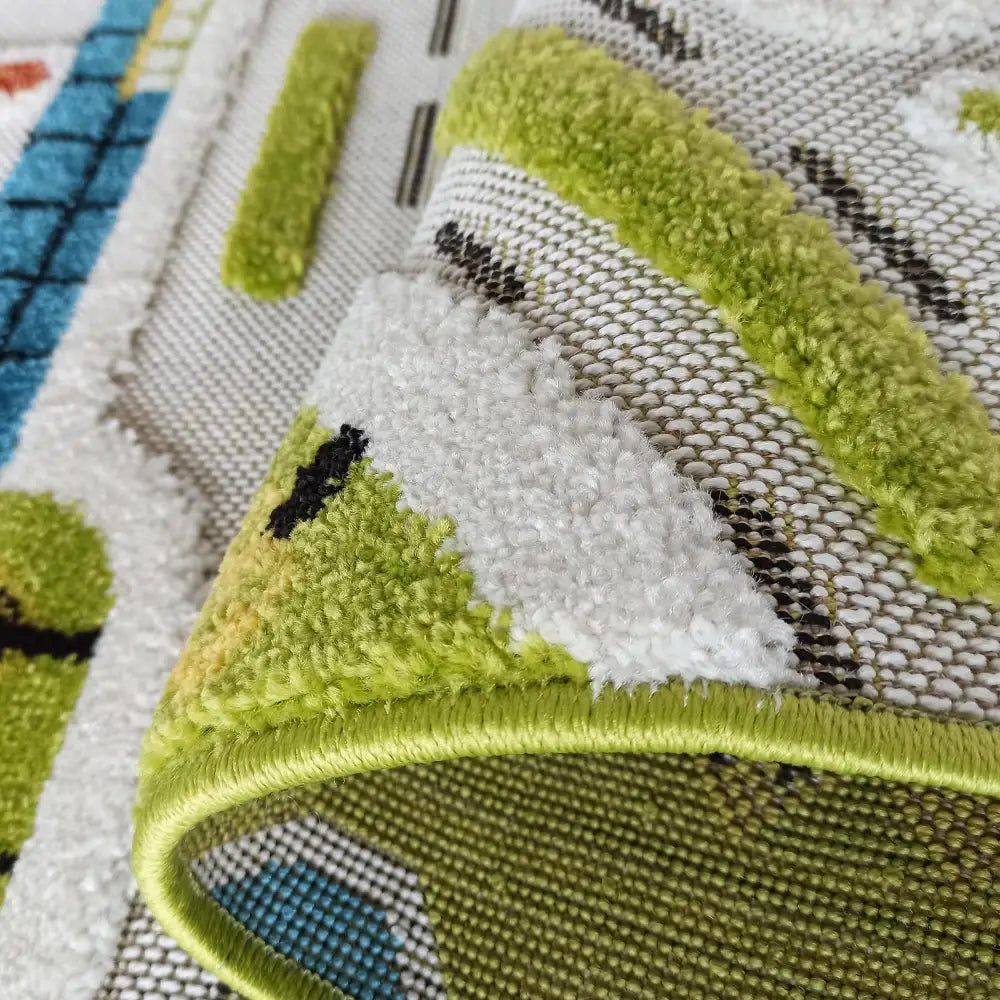 Tepe barneteppe i grønt, hvitt og blått, detaljert nærbilde med brettet kant som viser tykkelse og løkkestruktur.