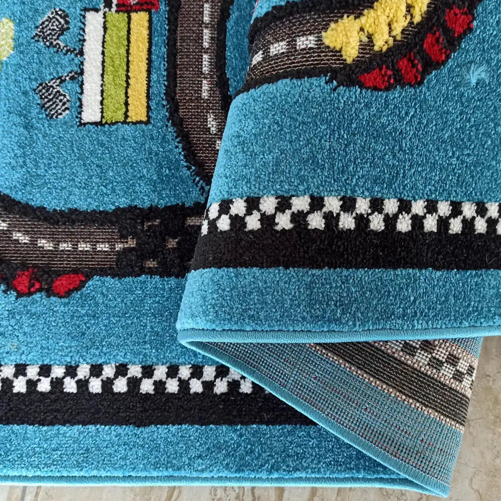 Blått barneteppe med bilbane-motiv, detaljerte farger og brettet kant som viser teppets bakside.
