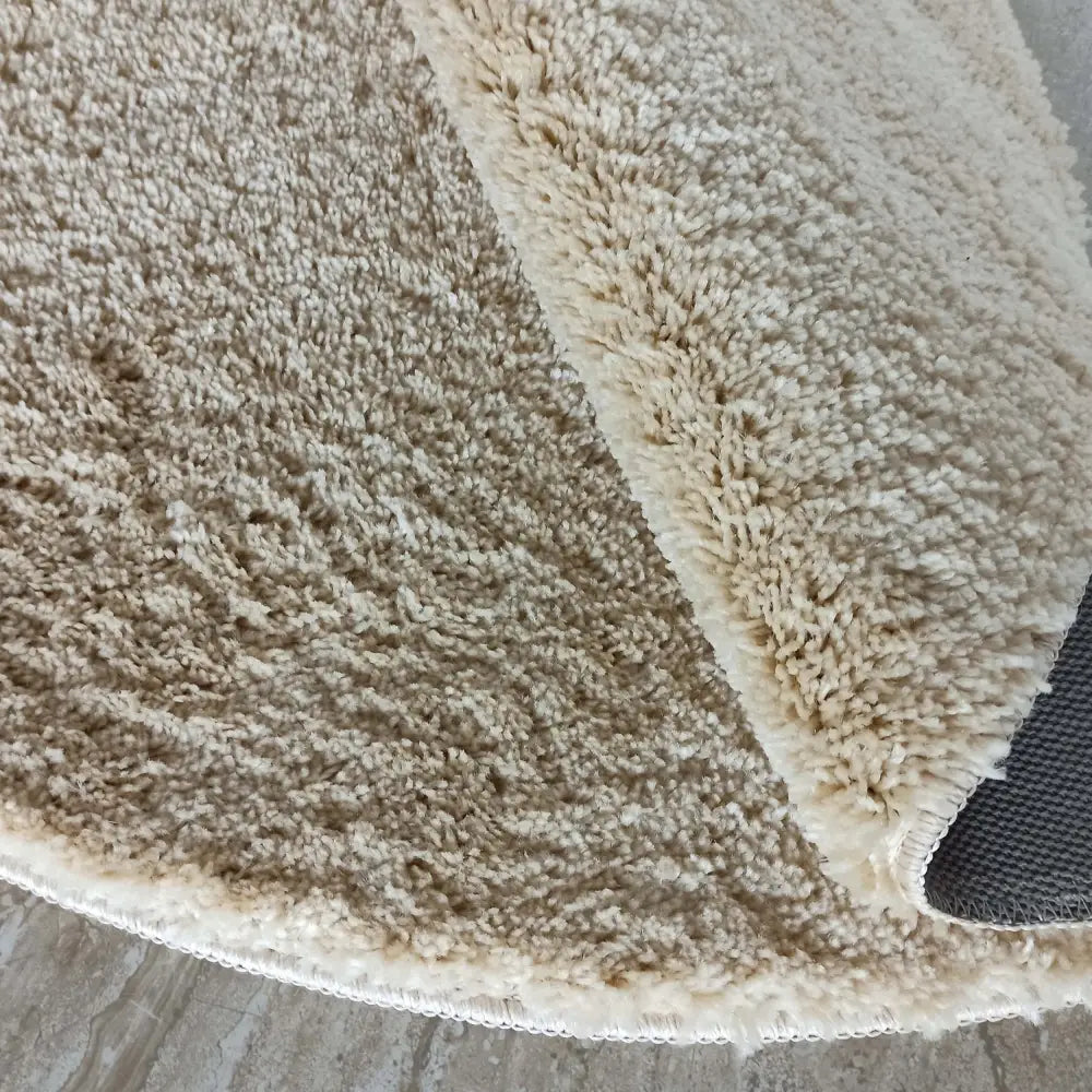 Tepe beige rundt teppe 140 cm, nærbilde som viser myk tekstur og undersiden ved oppbrettet kant.