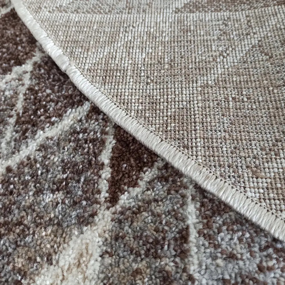 Tepe beige rundt teppe, detaljert nærbilde av brunmønstret luv og vevd beige bakside i hjørnet.