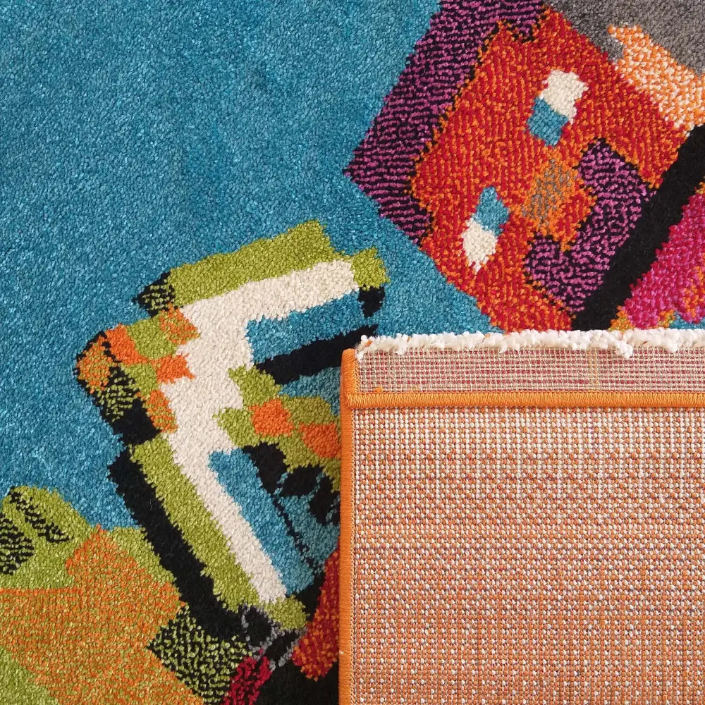 Tepe Bella 105 teppe, nærbilde med blå, grønn og oransje mønstre og synlig oransje kant på baksiden.
