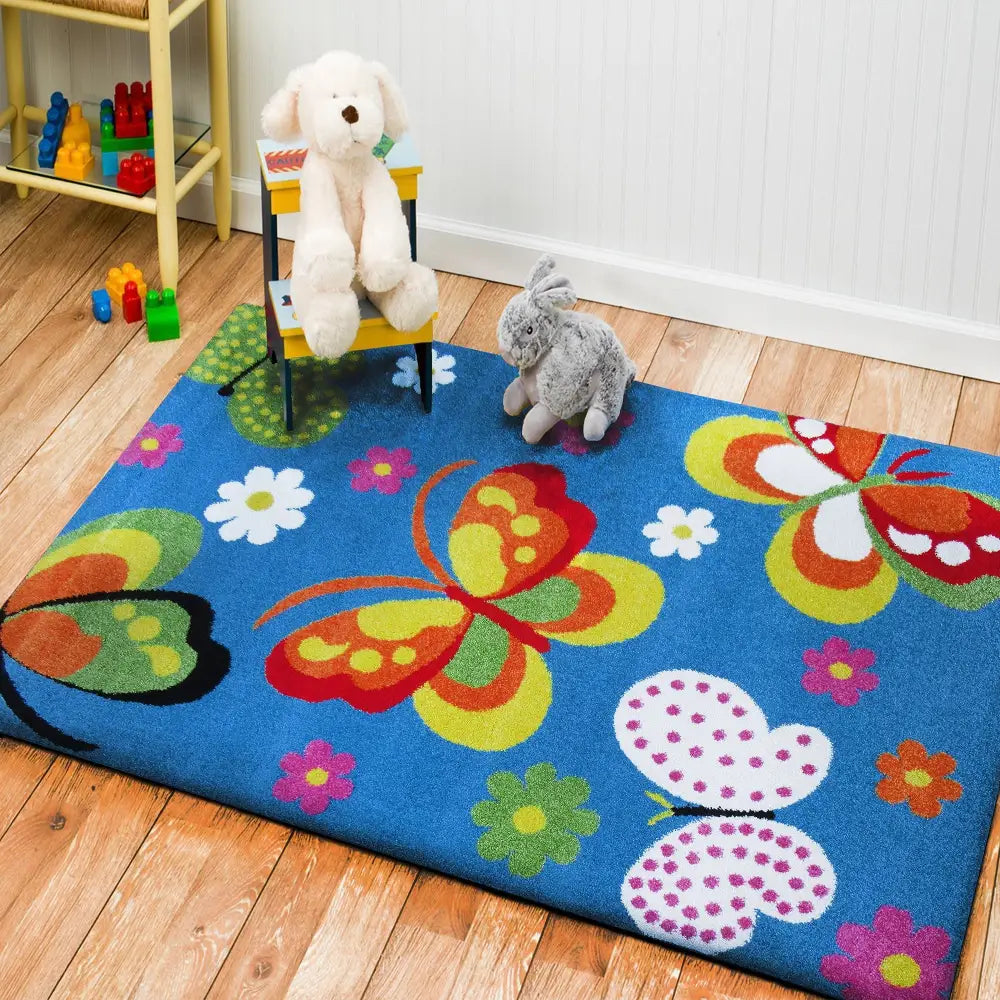 Tepe Bella 14 blått teppe med sommerfugler og blomster, barneromsmiljø med kosedyr og stol på tregulv.