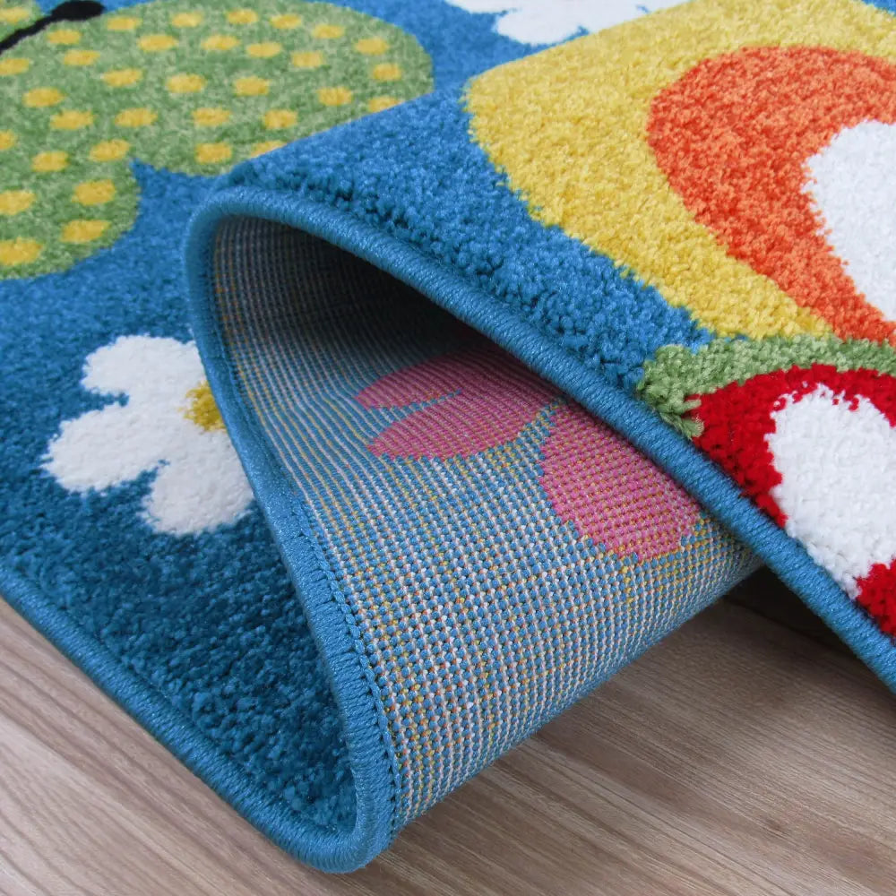 Tepe Bella blått teppe, nærbilde av blomstermønster og brettet hjørne som viser tykkelse og underside.