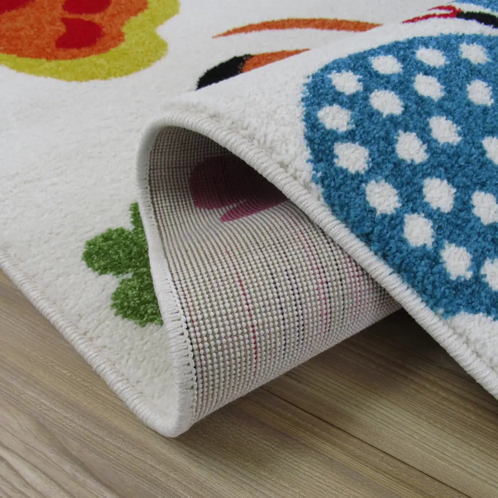 Tepe Bella 14 kremet teppe, nærbilde av hjørne med synlige blå prikker og brettet kant som viser baksiden.