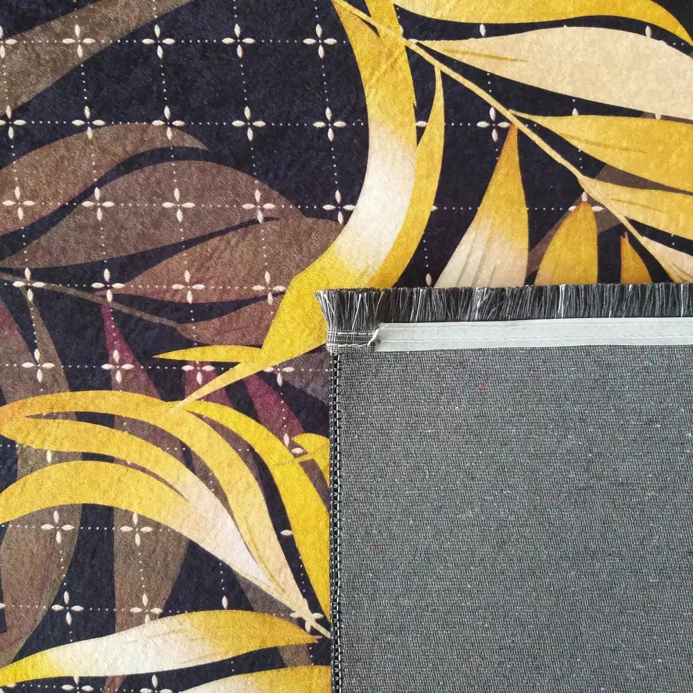 Tepe Black og Gold 08 teppe, nærbilde av hjørne med frynser og bladmotiv i gult, beige og mørkeblått.