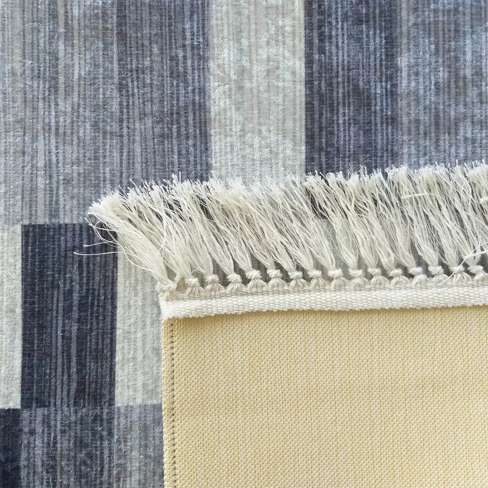 Tepe Blanka teppe i grått, nærbilde av hjørnet med beige bakside og frynser mot stripet underlag.