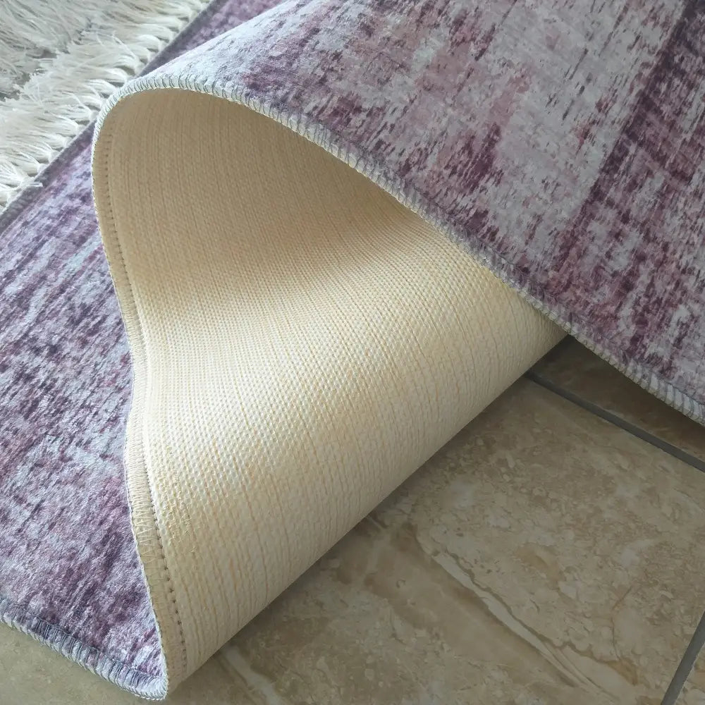 Tepe Blanka teppe i lilla og beige, sidevisning med oppbrettet hjørne som viser lys bakside og tekstur.