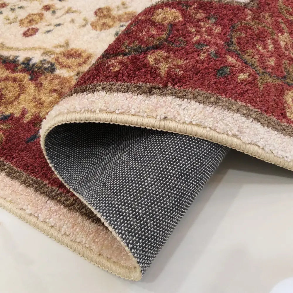 Tepe Casablanca teppe i rødt, beige og gult blomstermønster, detalj med brettet hjørne som viser grå underside.