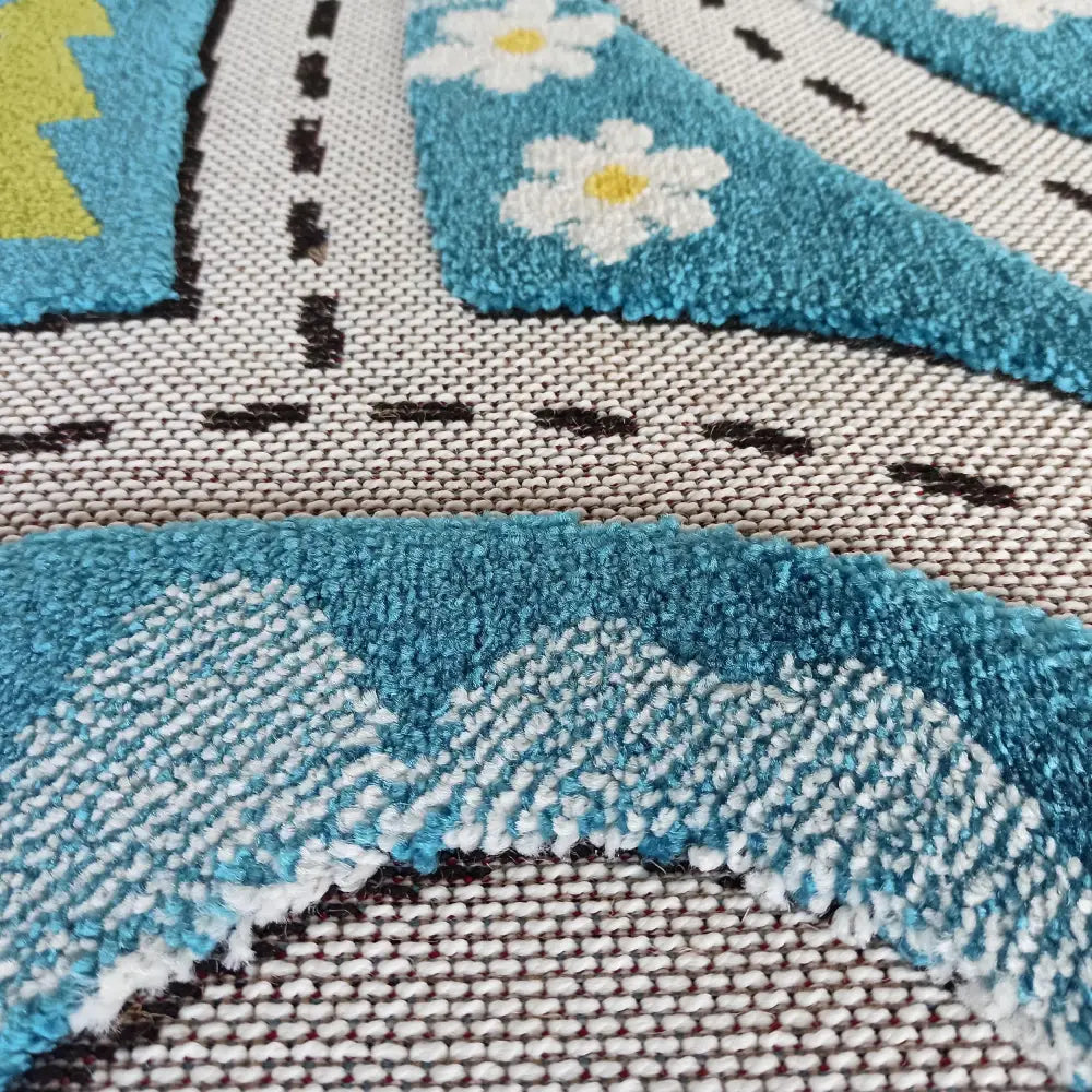 Tepe Color Kids 02 blått teppe, nærbilde av opphøyde blå og hvite blomster og stiplet svart linje på grovt underlag.