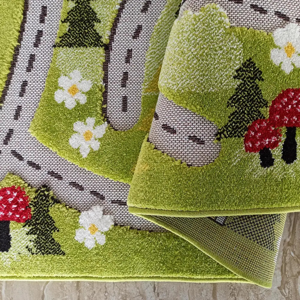 Tepe Color Kids grønt leketeppe, nærbilde av veimønster, blomster, trær og brettet hjørne som viser tekstur.