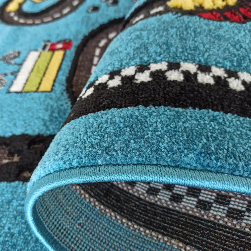 Tepe Color Kids teppe med blått bilbane-mønster, nærbilde av struktur, synlig kantsøm og oppbrettet kant.
