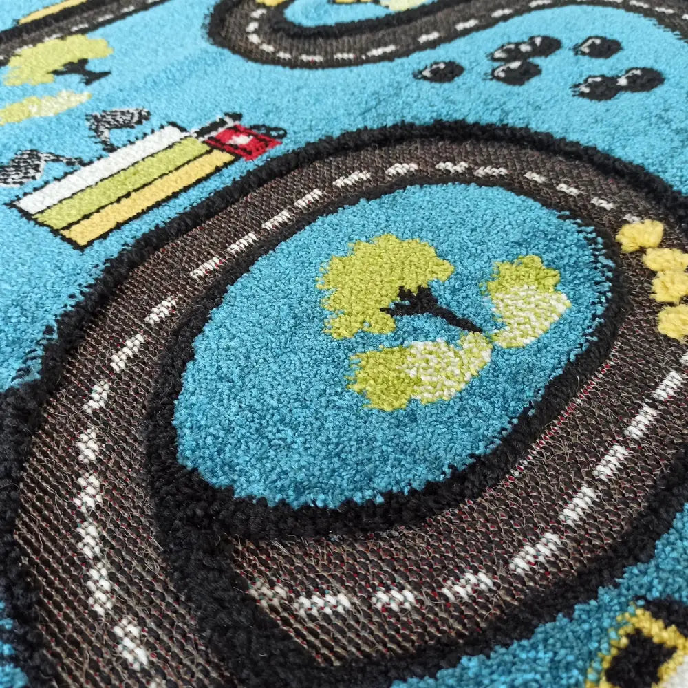 Barnerematte Tepe Color Kids, nærbilde av blå bakgrunn med svarte veier, grønne trær og fargerike bygninger.