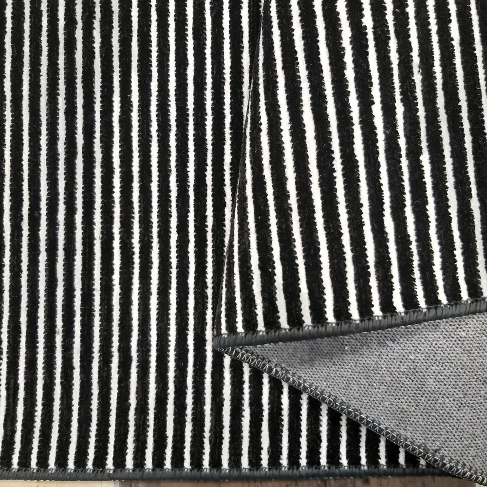 Tepe Diamond svart-hvit teppe, nærbilde av loddrette striper og oppbrettet hjørne som viser søm og underside.