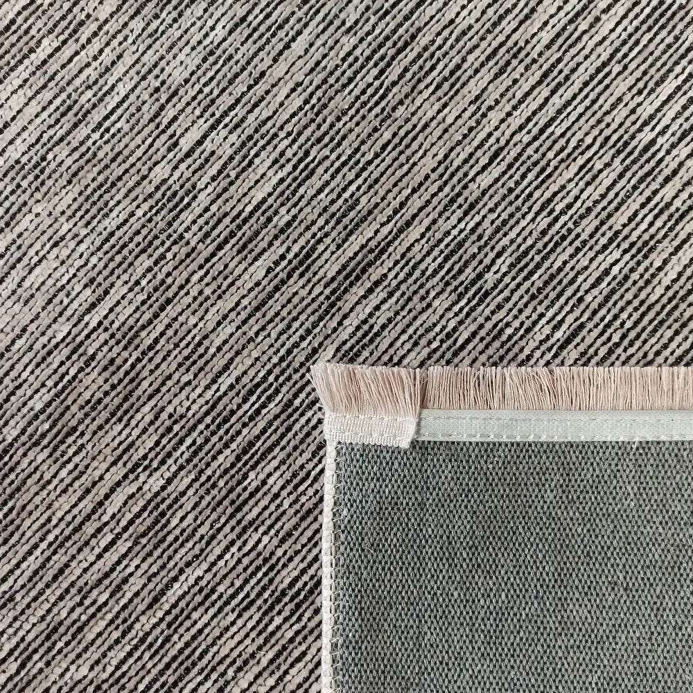 Tepe Diamond teppe i rosa, nærbilde av hjørnet med grå og svarte diagonale striper, frynser og grov bakside.