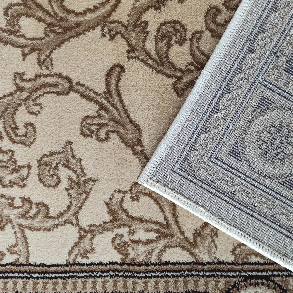 Tepe Eksklusiv 01 N krem, nærbilde av hjørne med lysebrunt mønster, synlig vevet bakside og lys kant.