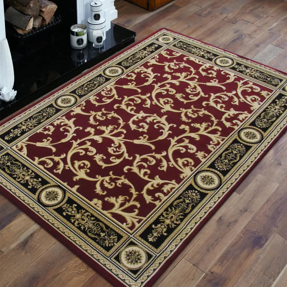 Tepe Eksklusiv teppe i vinrødt, klassisk ornamentmønster i gull og sort, plassert på tregulv ved peis.