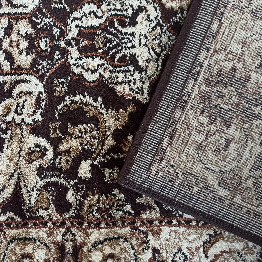 Tepe Eksklusiv teppe, nærbilde av hjørne med brettet kant som viser mønster og bakside i brune og kremtoner.