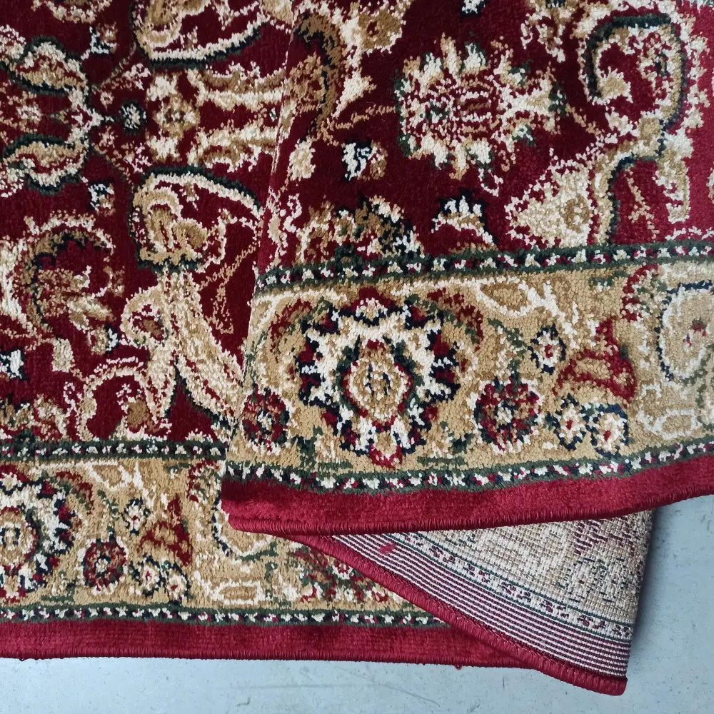 Tepe Eksklusiv teppe i rødt, orientalsk mønster, nærbilde av oppbrettet hjørne med synlig bakside.