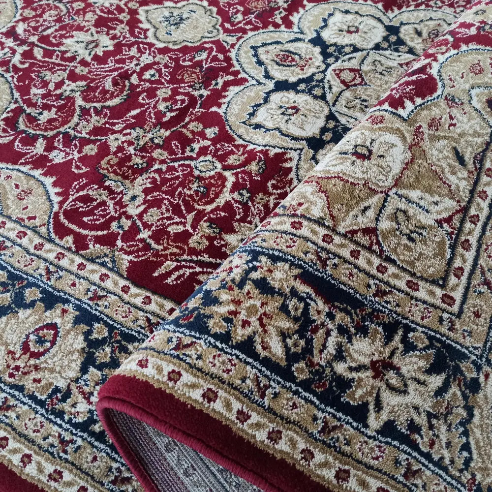 Tepe Eksklusiv 03 N teppe, nærbilde av brettet hjørne som viser rødt orientalsk mønster med blå og beige detaljer.