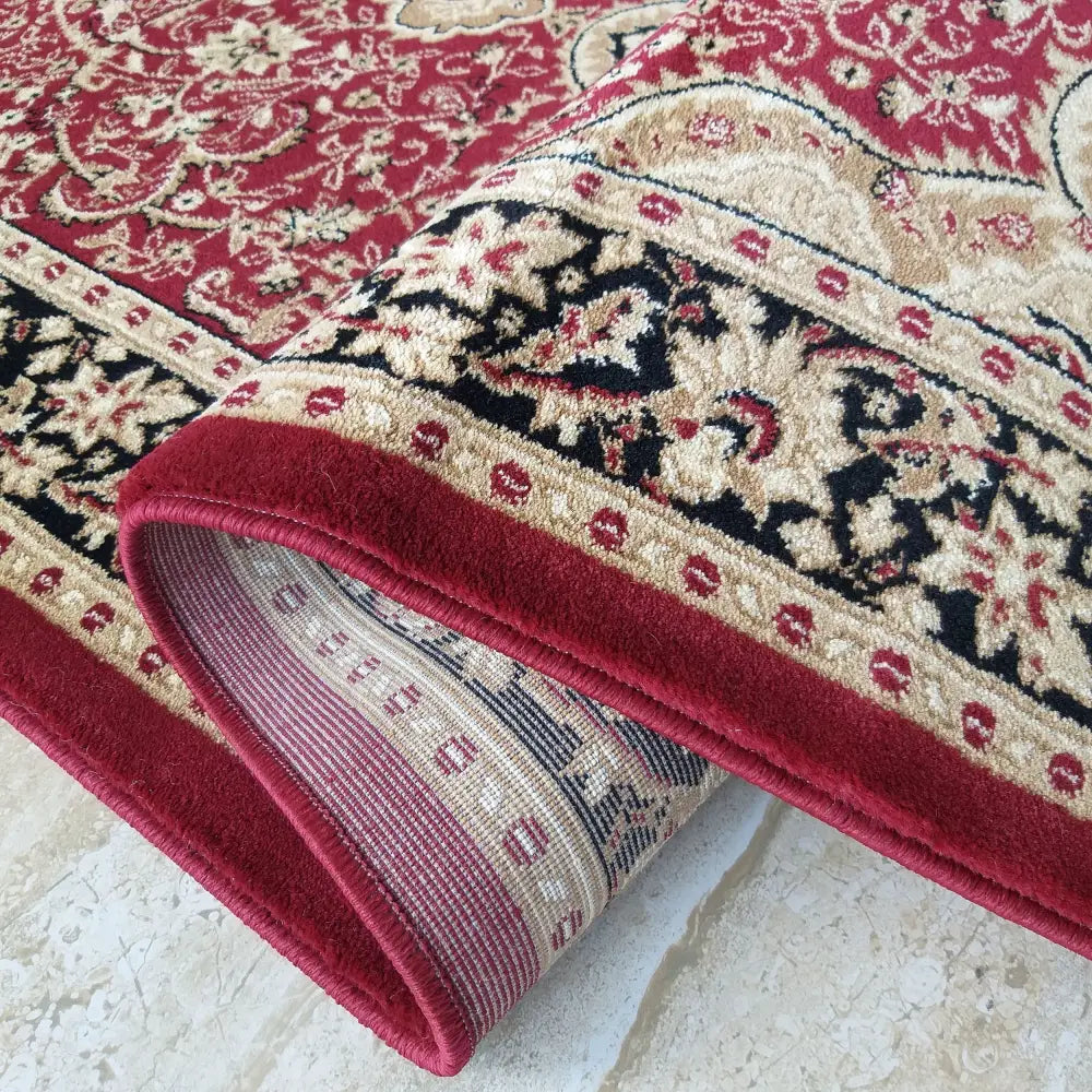 Tepe Eksklusiv teppe i rød, beige og svart orientalsk mønster, nærbilde med oppbrettet hjørne som viser baksiden.