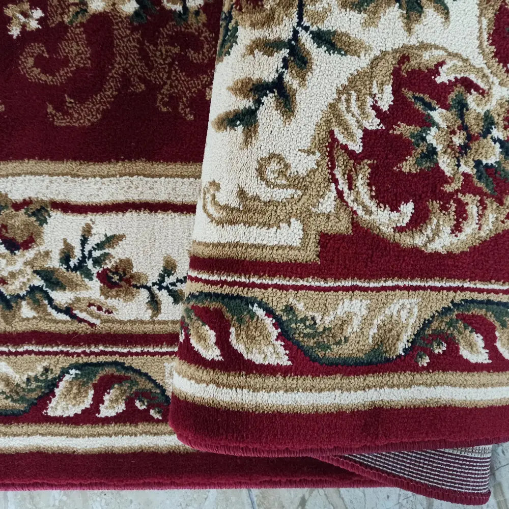 Tepe Eksklusiv 04 N teppe, nærbilde av burgunder blomster- og bladmønster med oppbrettet hjørne.