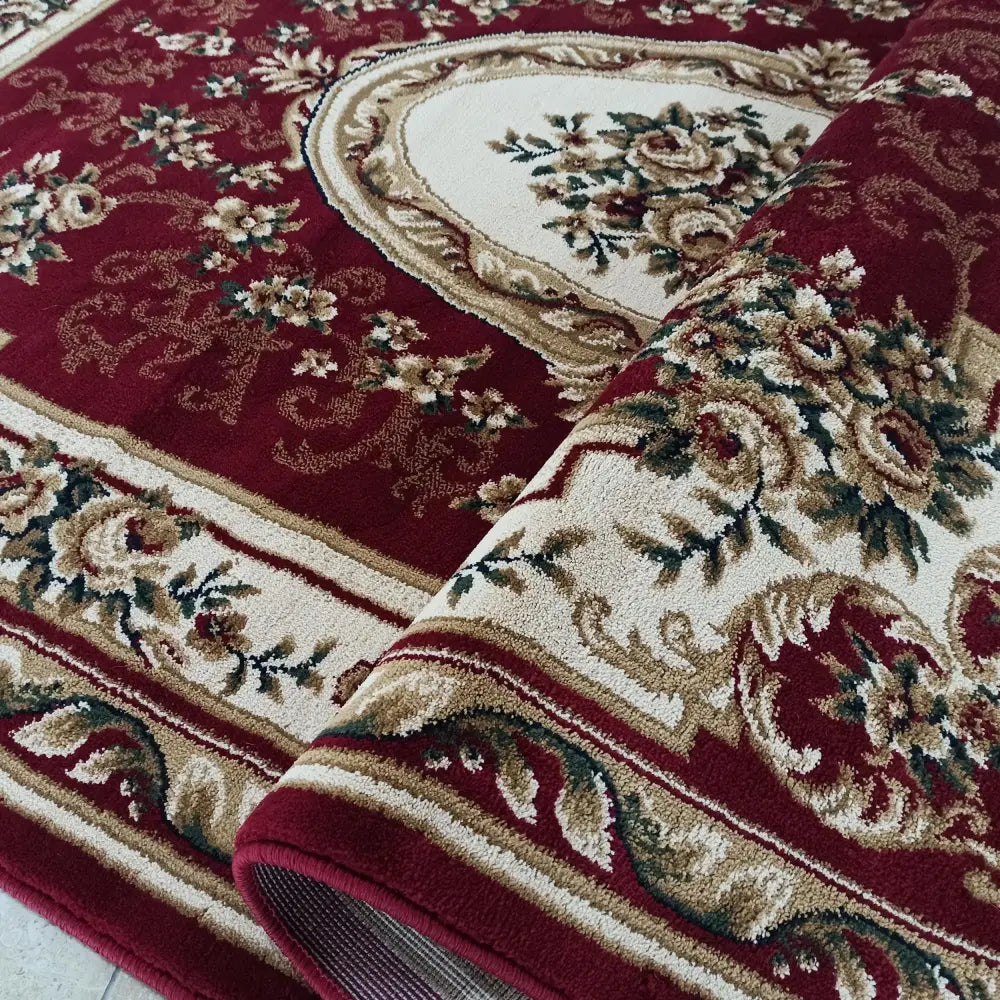 Orientalskinspirert teppe med rød bunn, kremhvite og beige blomsterdetaljer, delvis rullet sammen.