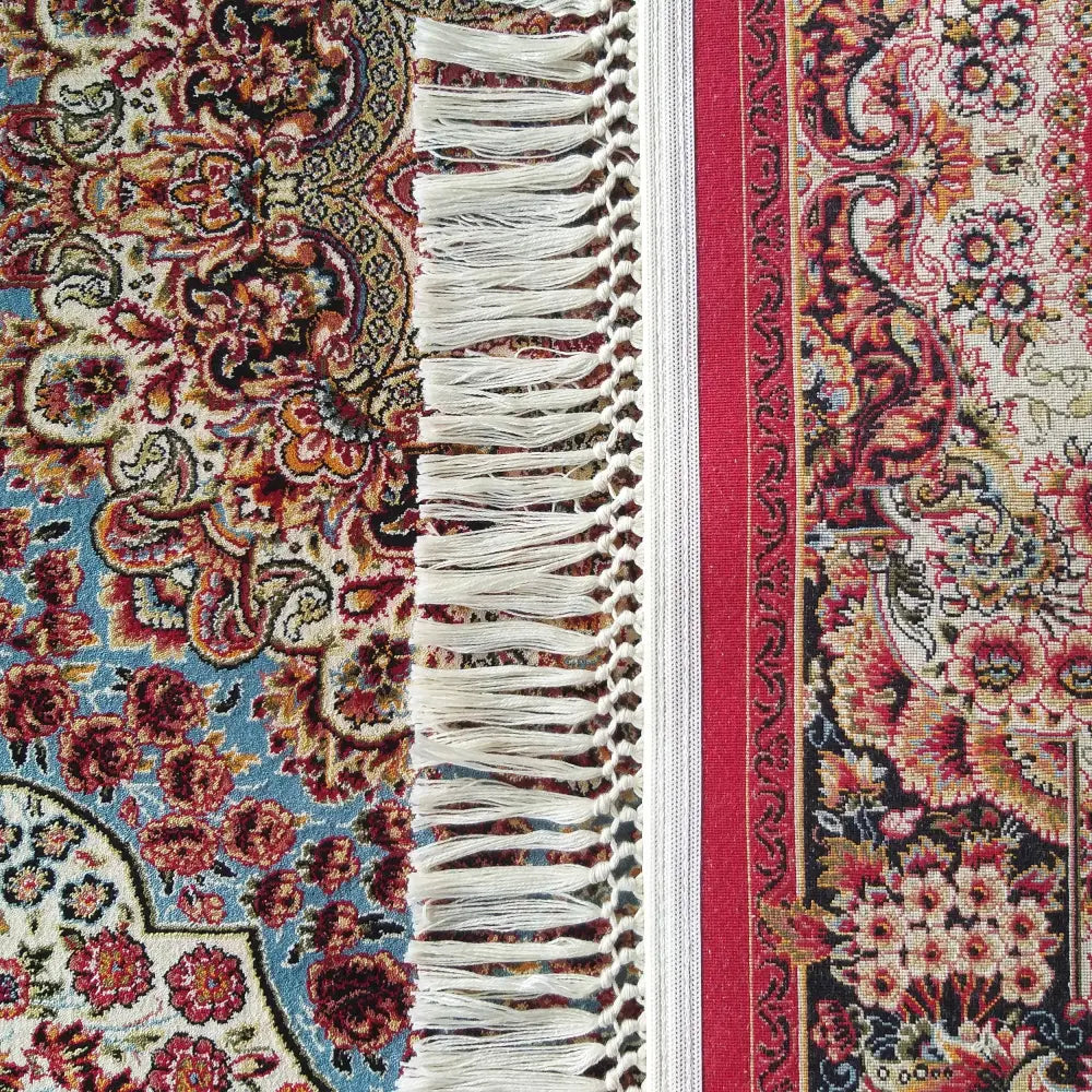 Tepe Eksklusiv teppe detalj, orientalsk mønster i rødt og blått nær hvite frynser og dekorativ bord.