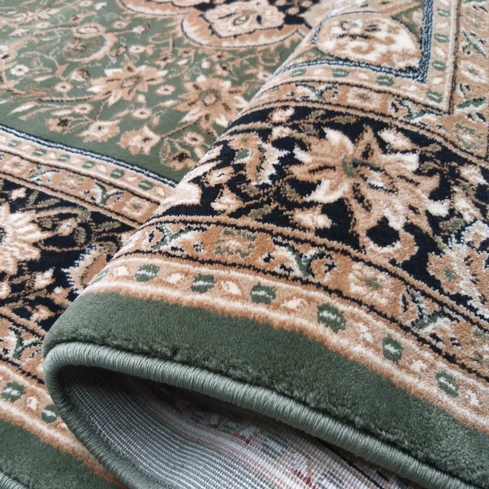 Tepe Eksklusivt teppe i grønt, nærbilde fra siden med opp-rullet hjørne som fremhever tykkelsen og mønsteret.