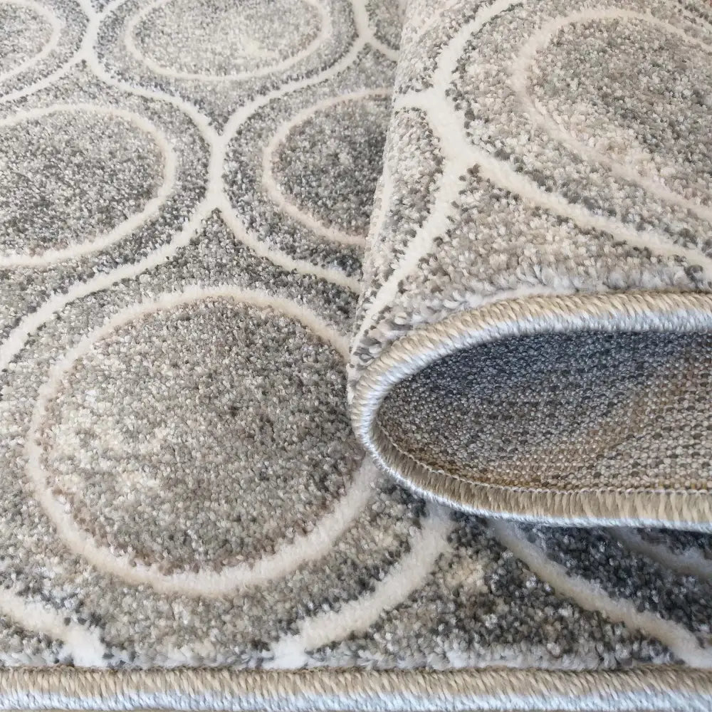 Tepe Enigma teppe i grått, nærbilde av sirkelmønster og brettet kant som viser tykkelse og tekstur.