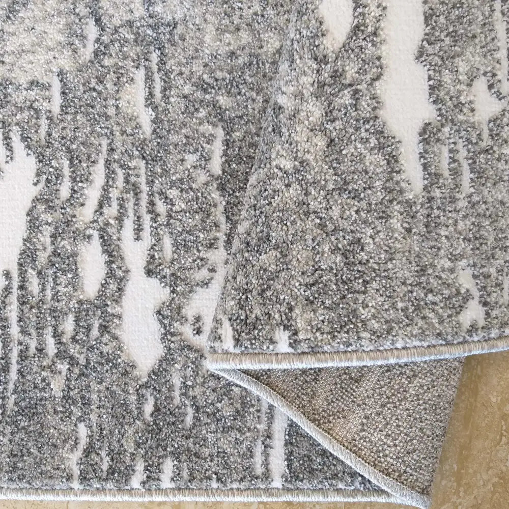 Tepe Enigma grått teppe 200 x 290 cm, nærbilde av abstrakt mønster og oppbrettet kant som viser undersiden.