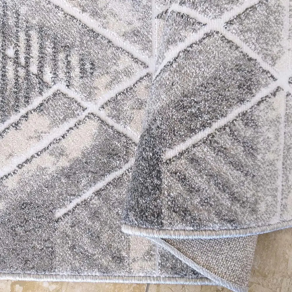 Tepe Enigma teppe grått og hvitt, nærbilde av geometrisk mønster med synlige hjørner og materialets underside.