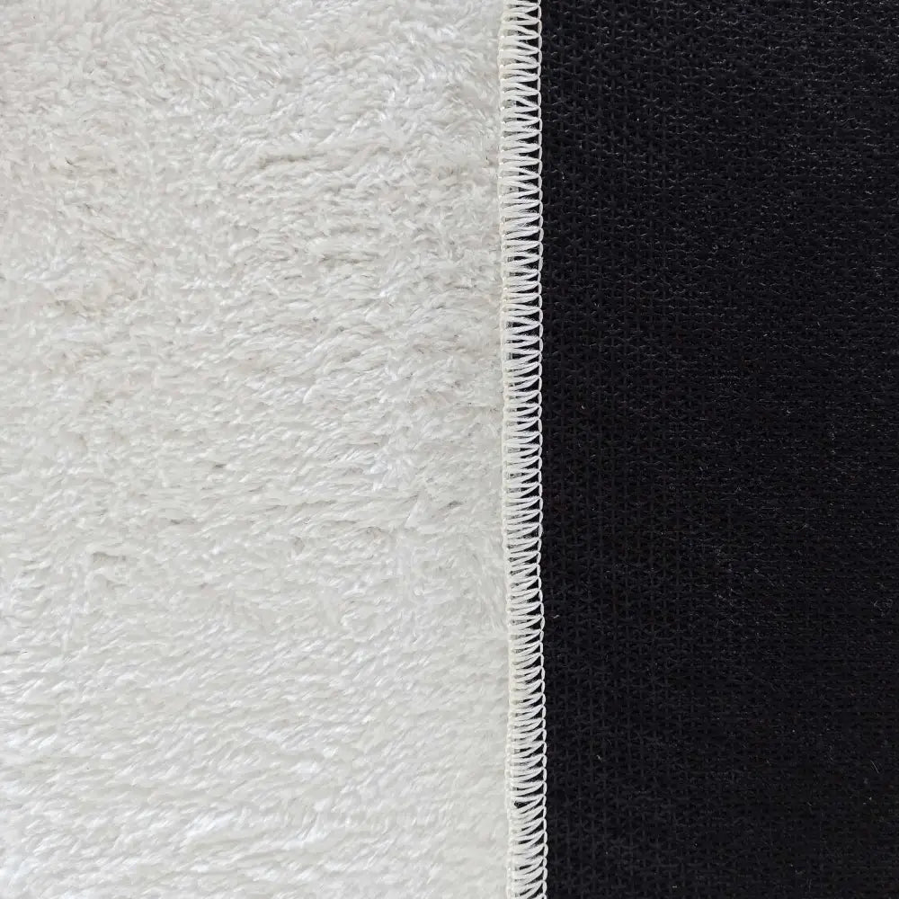 Tepe Enzo kremfarget teppe, nærbilde av sømmen mellom hvit frotté og svart glatt stoff.